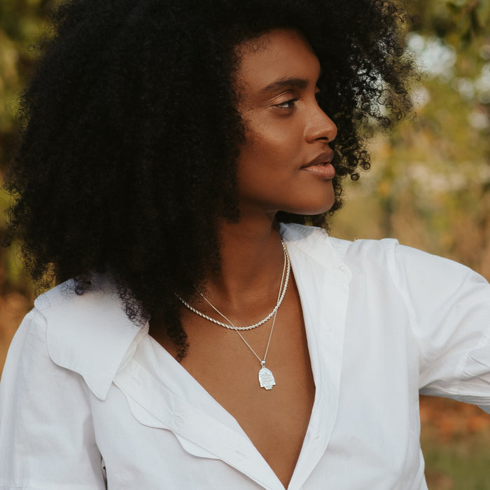 A woman with curly hair in a with top wearing two silver necklaces