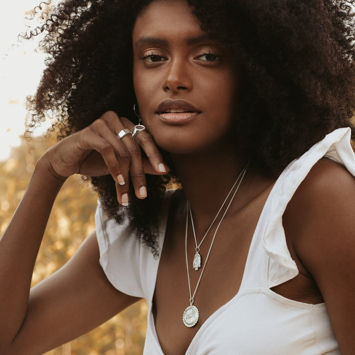 A woman with curly hair in a with top wearing two golden necklaces and rings