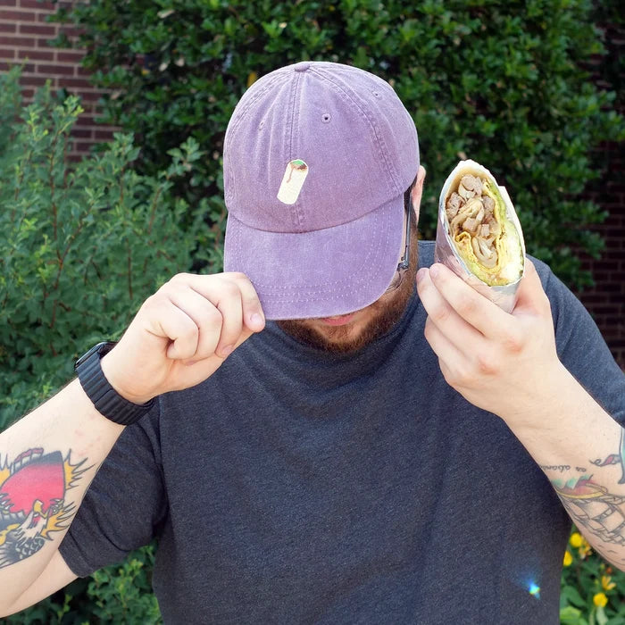 Image of man wearing purple embroidered dad hat holding a breakfast burrito