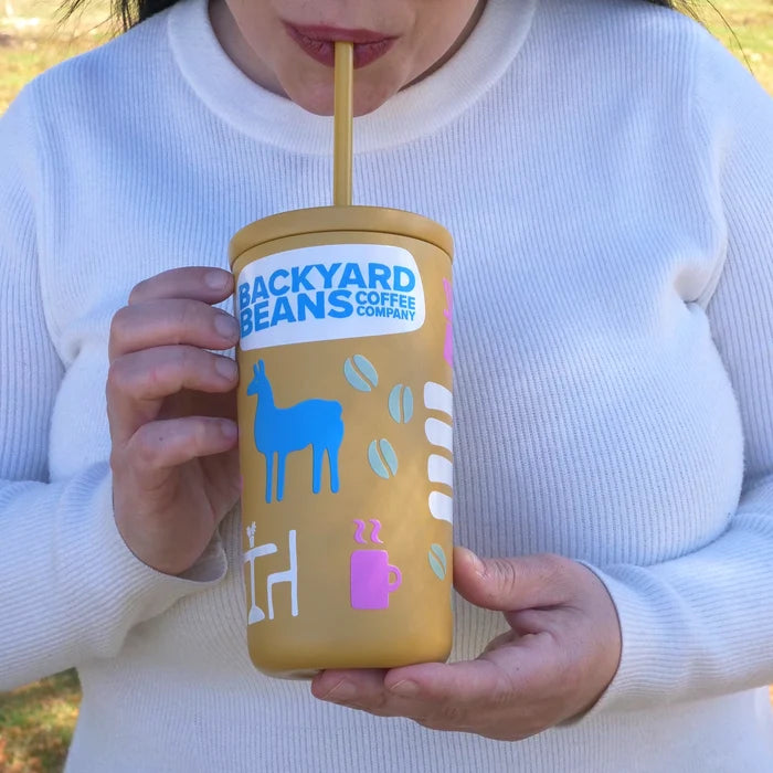 Person sipping a yellow 'Backyard Beans Coffee Company' tumbler with a straw.