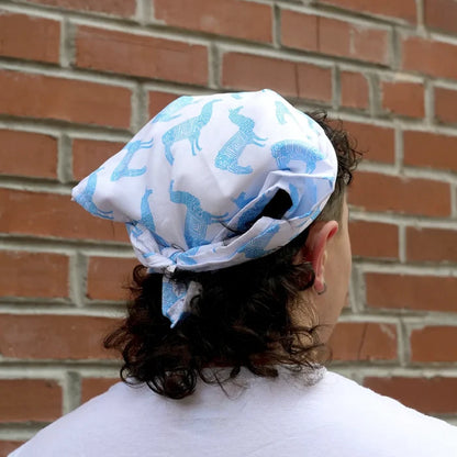 Person wearing a white headscarf with blue llama pattern against a brick wall