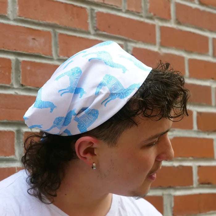 Person wearing a white headscarf with blue llama pattern against a brick wall.