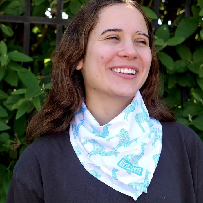 Person wearing a light blue llama patterned scarf standing outdoors against green foliage.