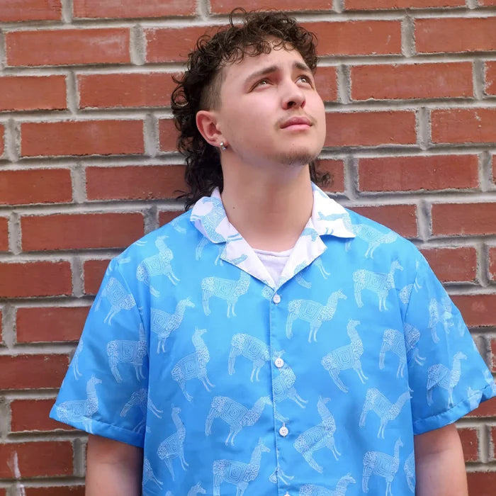 Person wearing a blue shirt with llama pattern against a brick wall