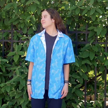 Person wearing a blue llama patterned shirt in front of green foliage