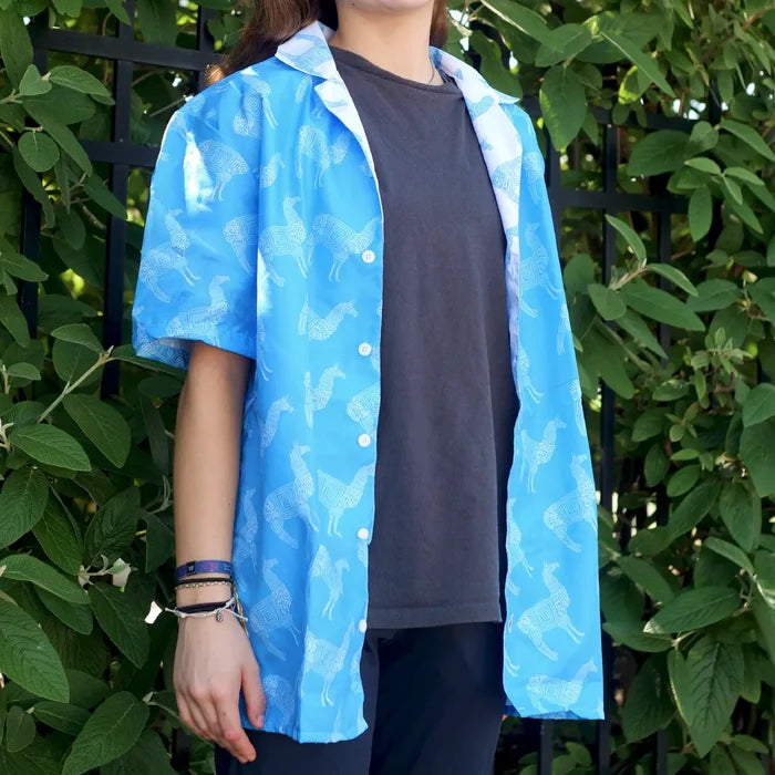 Person wearing a blue llama patterned shirt over a dark top against a green leafy background