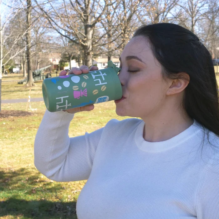 Woman drinking from a green tumbler with a colorful design outdoors.