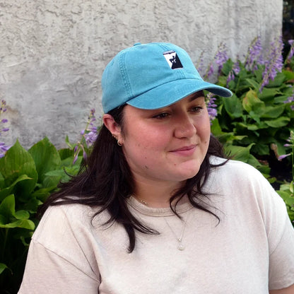 Image of woman wearing blue hat with embroidered can with green background