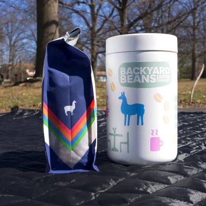 Backyard Beans reserve canister and retail coffee bag on a black surface with trees in the background