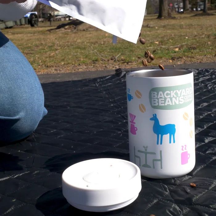 Reserve Canister with 'Backyard Beans' branding on a black surface outdoors being filled with coffee beans.