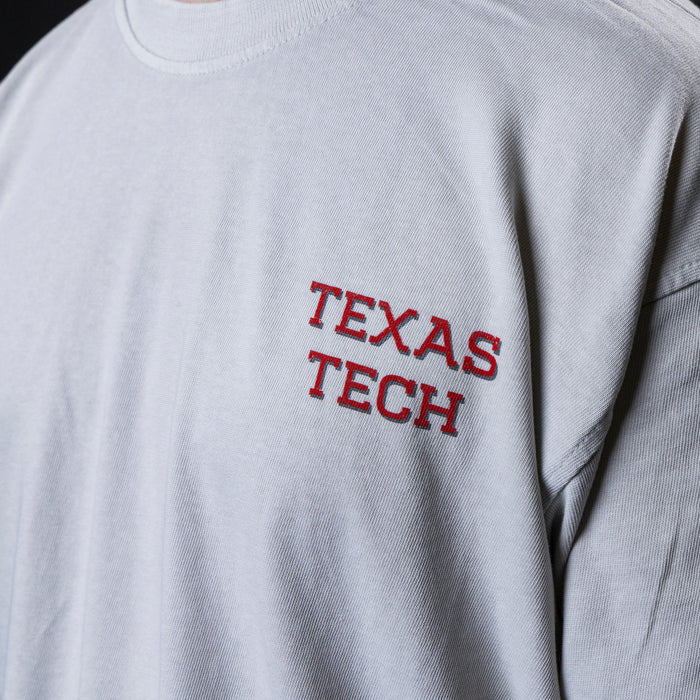 Close-up of a light gray t-shirt featuring 'TEXAS TECH wordmark screen-printed on the left chest