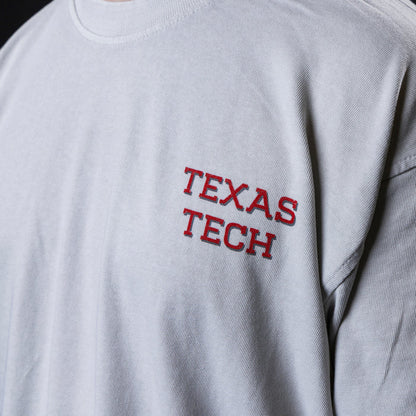 Close-up of a light gray t-shirt featuring 'TEXAS TECH wordmark screen-printed on the left chest